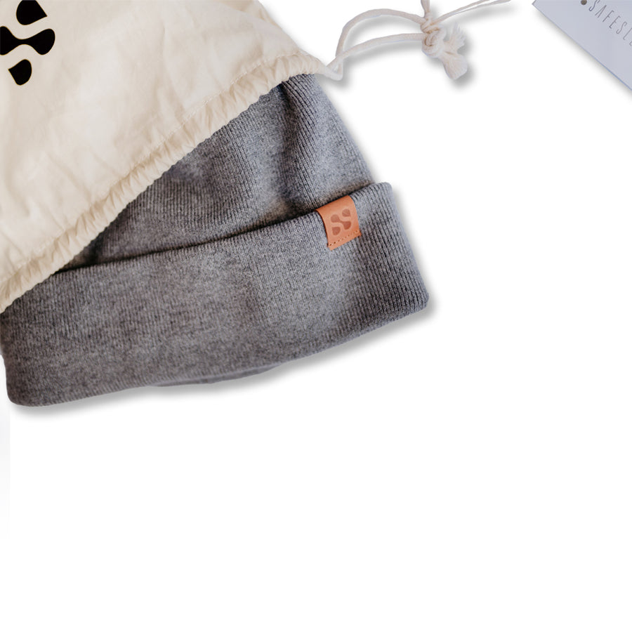 Gray beanie with a small leather tag, designed to block RF radiation, shown partially covered by a beige drawstring bag.