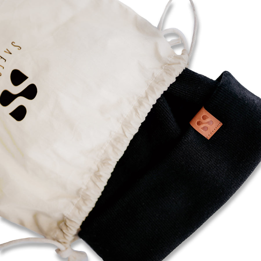 Black beanie with a pink label and a white drawstring bag, designed to block radio frequency signals.