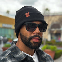 Man wearing a black RF blocking beanie and sunglasses outdoors, dressed in a plaid shirt and white t-shirt.